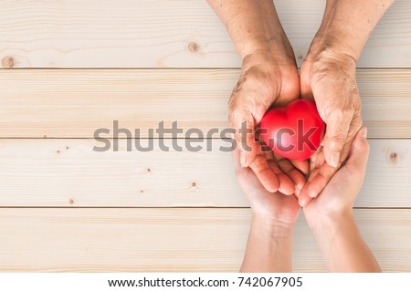 Elderly senior person or grandparent\'s hands with red heart  in support of nursing family caregiver for national hospice palliative care and family caregivers month concept
