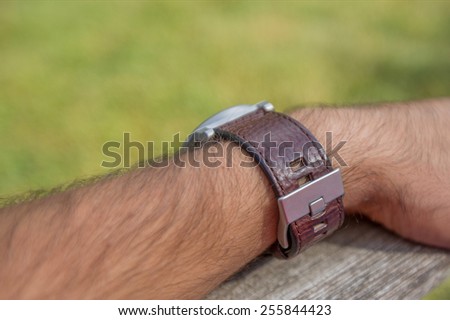 Sitting man's arm wearing brown leather watch