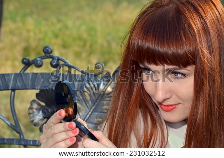 Haired girl looking in a small mirror on a background of nature
