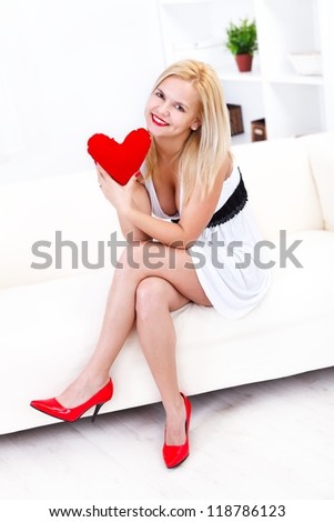 Sexy woman sitting on sofa with red heart in hand