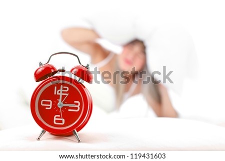 Sleepy woman lying in bed with alarm clock in front