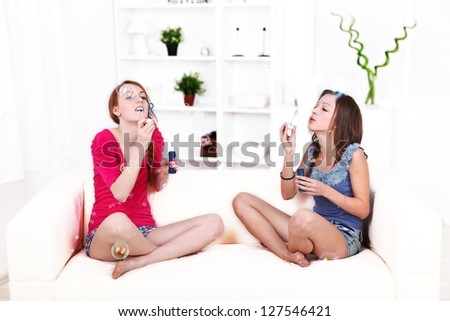 Picture of pretty girls sitting and blowing soap bubbles at home