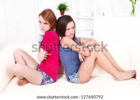 Two upset girl sitting back to back to each other in quarrel