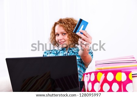 Woman with laptop and shopping bags showing a credit card to the camera