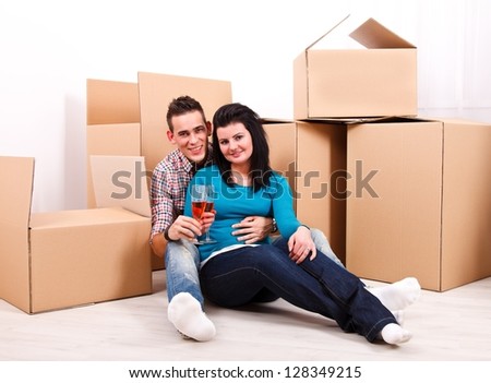 Young couple celebrating moving into their new home toasting with red wine in front of moving boxes