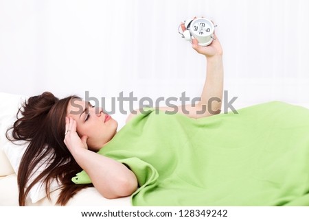 Sleepy woman lying in bed with alarm clock in hand