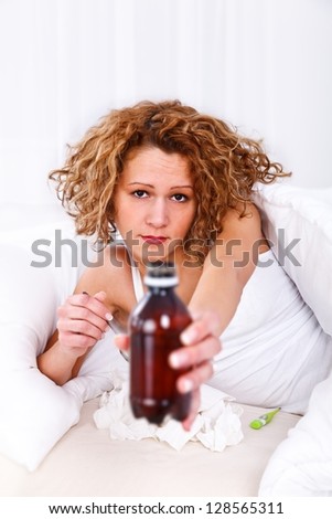 Sick young woman in bed showing cough syrup to the camera