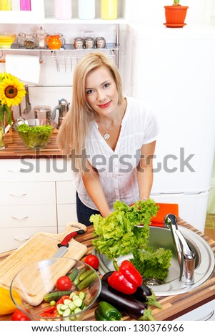 Happy smiling young woman in the kitchen with vegetables making healthy dinner