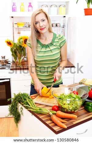 Attractive young woman cutting vegetables, preparing a healthy food in the kitchen