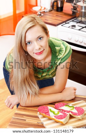 Portrait of a lovely blonde woman with long hair in the kitchen, having two sandwiches in front of her