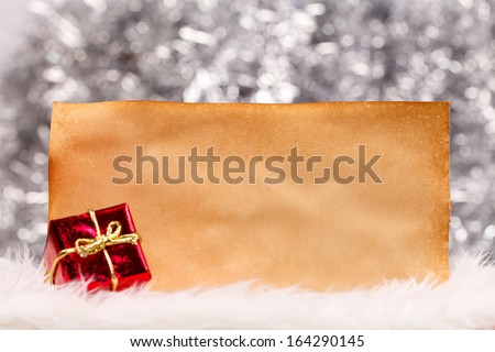 Gift box and old sheet of paper on silver blurry christmas light background.