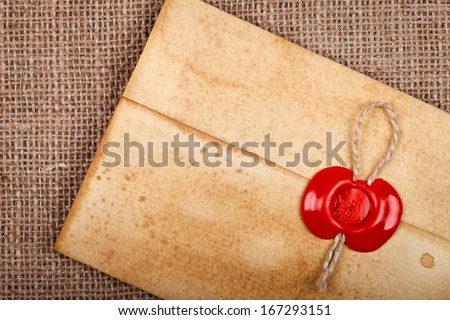 Detail of old grunge envelope with red wax seal on hessian sacking burlap background.