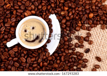 Cup of coffee with smiley face on coffee beans and burlap background