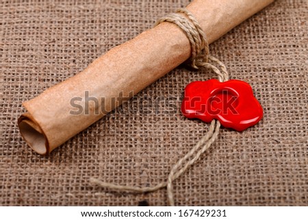Old paper scroll with empty red wax seal on burlap background.