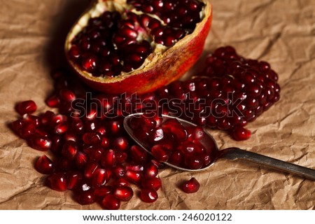 Pomegranate seeds and fruit with silver teaspoon on rustic paper
