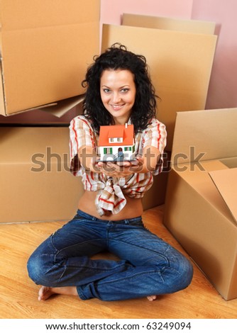 Attractive young woman offering a miniature house, boxes in the background