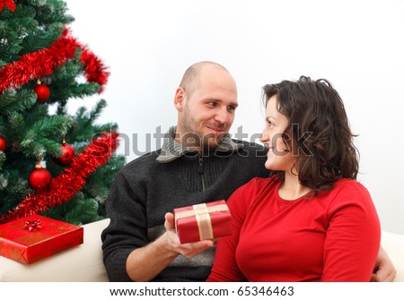 Young man giving a gift to his girlfriend near the Christmas tree