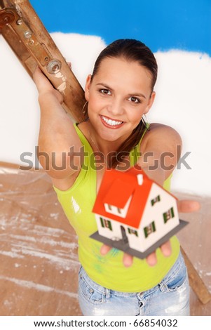 Attractive woman worker at the ladder offering a  miniature house to us, focus on the woman