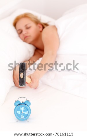 Lazy woman is smashing the alarm clock with a hammer from the bed