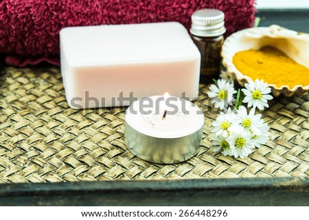 Spa concept with aromatic essence,soap and turmeric powder on tray decorated by cutter flower and lit tea candle decorated by cutter flower and lit tea candle
