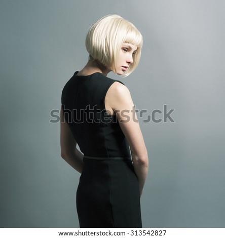 Beautiful skinny slender young blond girl in a wig is back in the studio in a strict black dress back