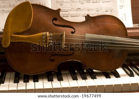 Old violin lying on a piano keyboard with sheet music behind