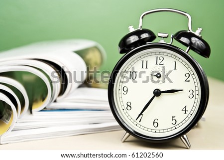 Open magazines in composition with vintage clock lying on table on green background