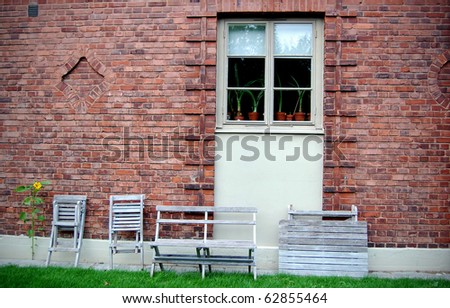 wall from a red brick, by a window a wooden garden furniture