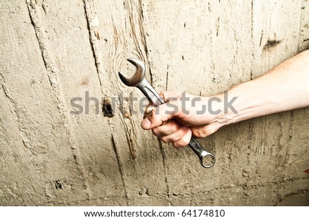 Hand with a wrench on concrete background