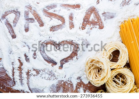 Pasta composition with pasta text and heart written flour on wooden rustic table top view