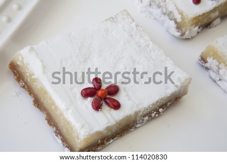 Closeup of one lemon bar with red candy flower accent placed on white glass tray.