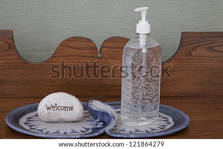 Decorative Display of Hand Sanitizer on antique carved hall table with Welcome sign on blue design plate. Grass Cloth wall decor