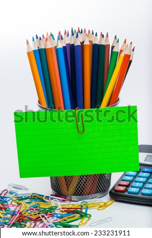 Colored pencils in a cup, with an index card paper clipped to the cup. Calculator and colored paper clips in the image as well