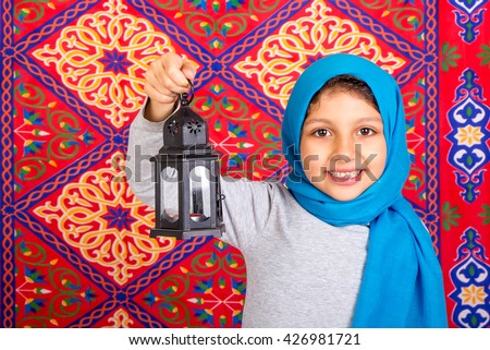 Ramadan Kareem - Happy Young Muslim girl celebrating Ramadan , holding Ramadan lantern in front of Islamic Arabian fabric traditional background