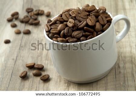 a mug overflowing with rich dark roasted whole coffee beans. shallow dof