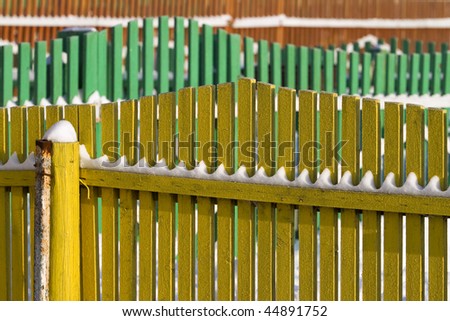 perspective shot  several  wooden fences, of different color, covered with snow.
