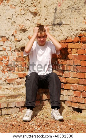 young guy in depression condition, sits against a brick wall