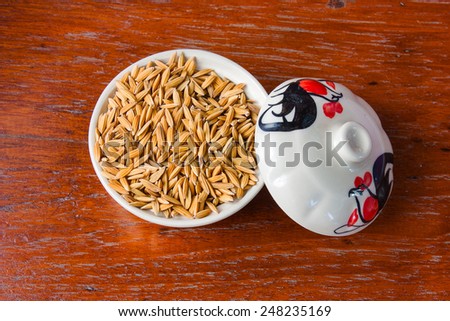Paddy seeds in a cup of white coating on the wooden floor.