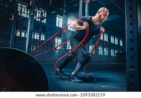 Men with battle rope battle ropes exercise in the fitness gym. CrossFit concept.