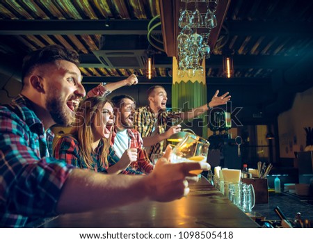 Sport, people, leisure, friendship, entertainment concept - happy male and female football fans or good yuong friends drinking beer, celebrating victory at bar or pub. Human positive emotions concept
