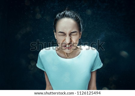 Young funny woman sneezing with spray and small drops, studio portrait on black background. Comic, caricature, humor. illness, infection, ache. Health concept