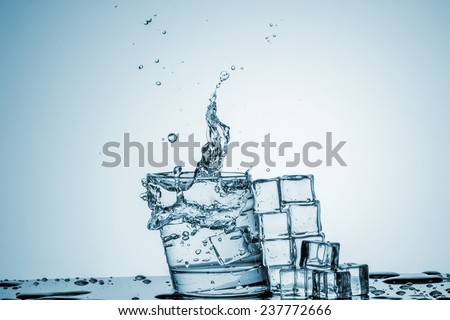ice cubes falling into a glass of water and ice cubes, lying next, on blue background