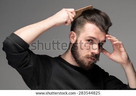 young man comb his hair on gray background