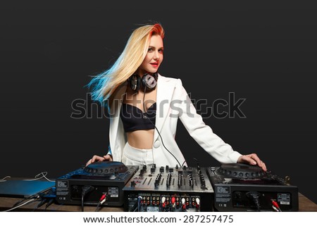 Beautiful blonde DJ girl in a white suit on decks on the party on the black background