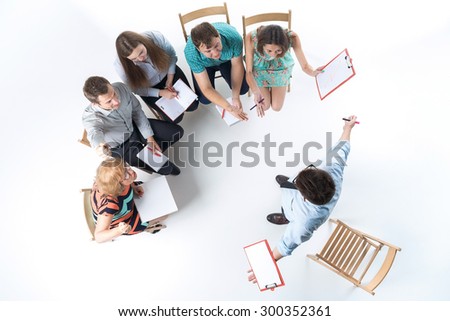 Top view of business people in a meeting on white background. all sitting with notepad and pen. speaker standing and spreading his arms
