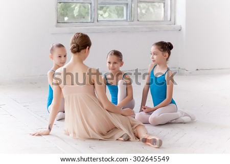Three little ballerinas with personal ballet teacher in dance studio. classic ballet dancer as teacher sitting in a white studio