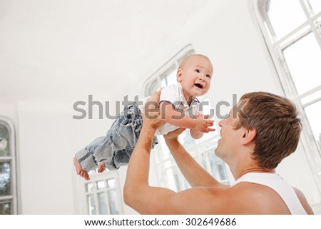 Young smiling father with his nine months old son playing at home on white home background. father throwing up his son