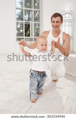 Young smiling father with his nine months old son learning to walk at home on white home background