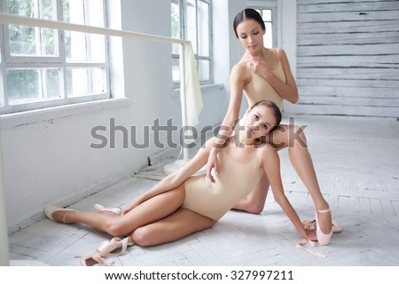 The two classic ballet dancers sitting and posing on white wooden floor