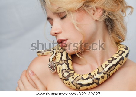 Beautiful blonde girl and python around her body on gray background